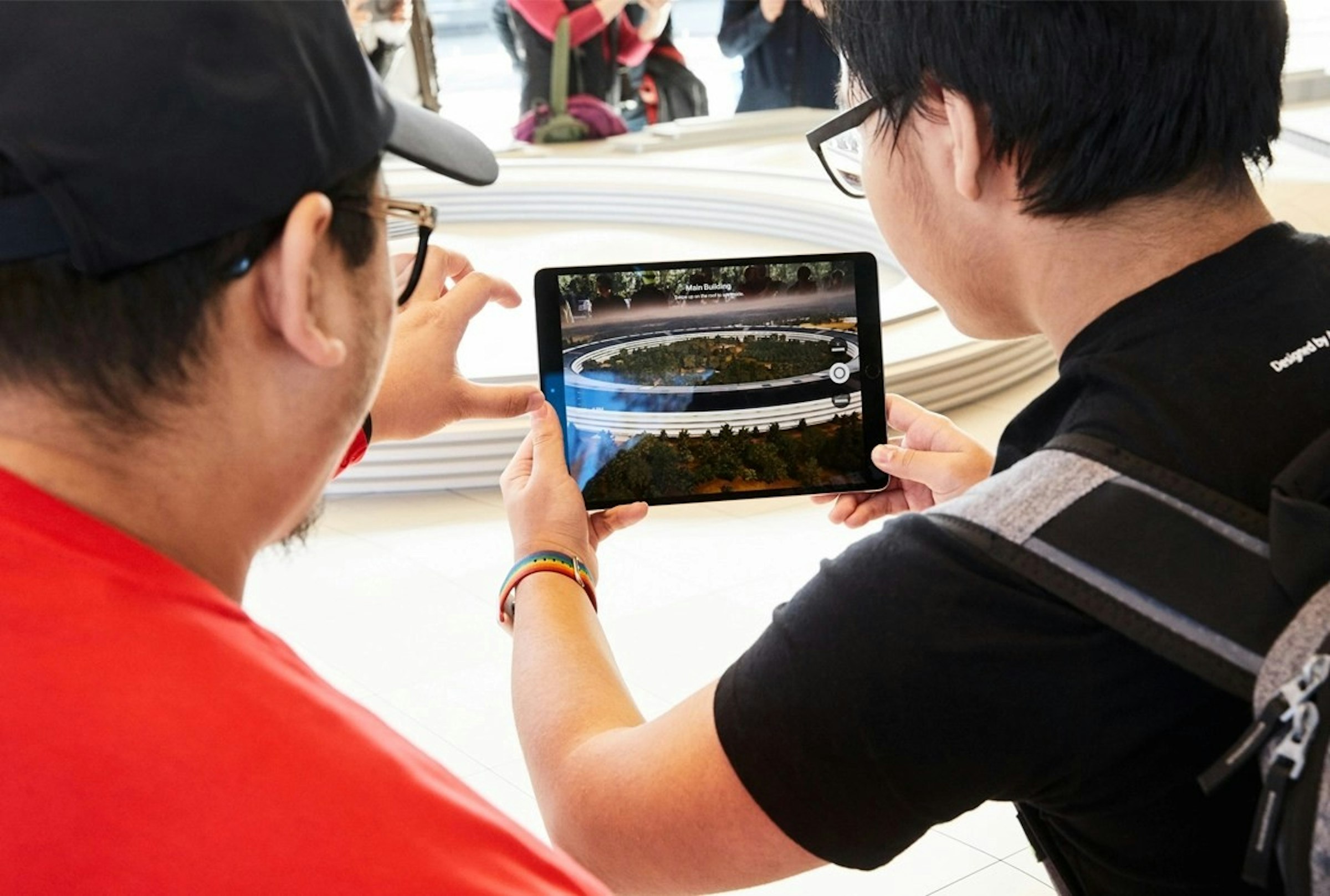 照片中提到了Main Building、the、Designed by A，包含了蘋果公園遊客中心、蘋果園、Apple Apple Park 遊客中心、蘋果、T恤衫